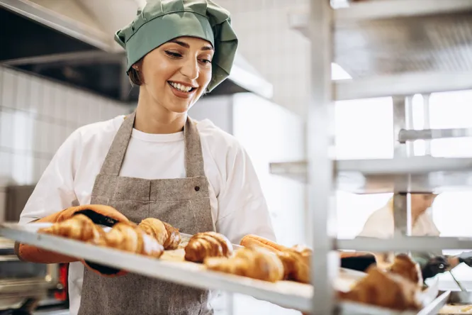 Bäckerin trägt ein Blech mit frisch gebackenen Croissants