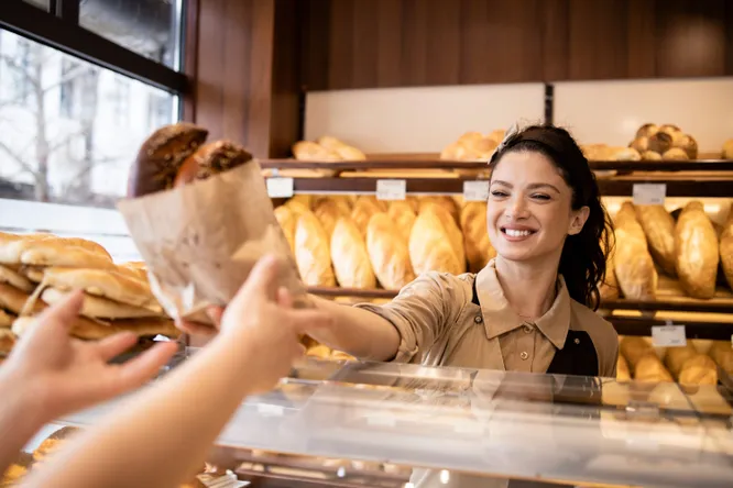 Bäckerin reicht Brot über die Verkaufstheke